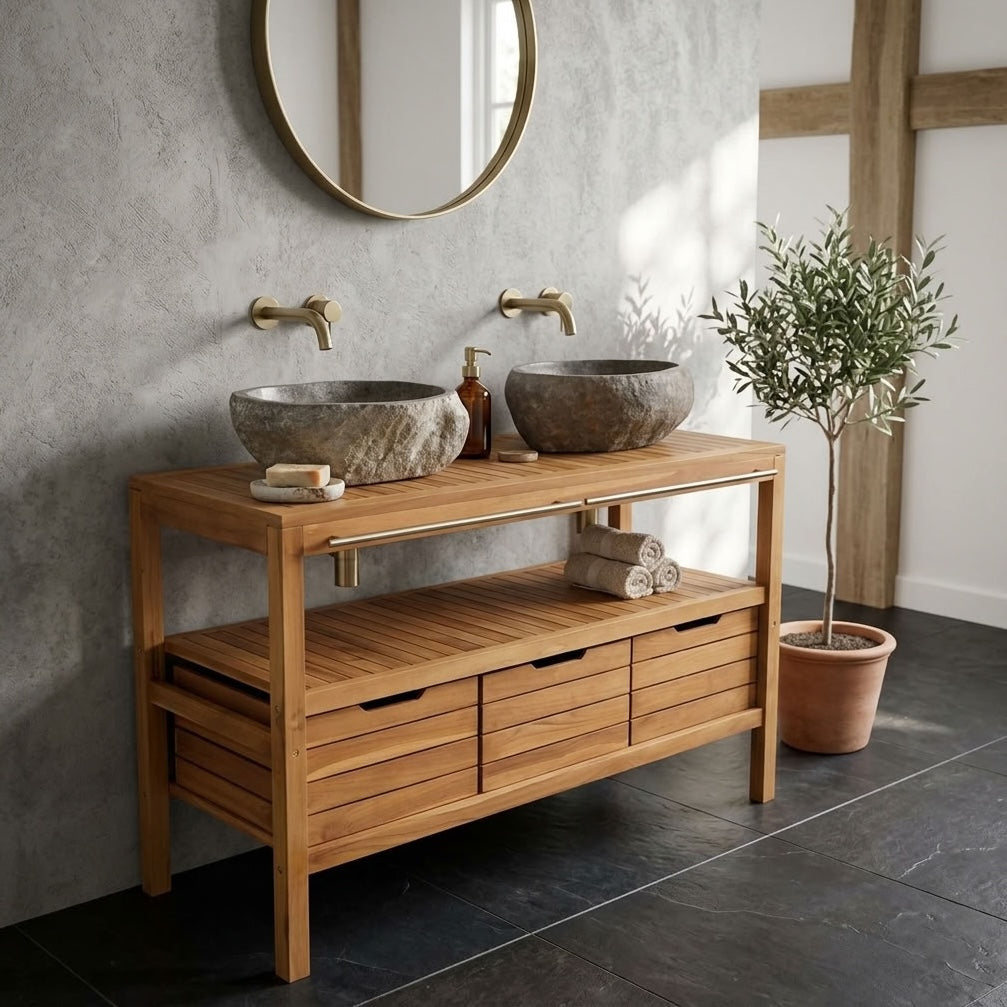A teak wooden bathroom vanity unit with two stone vessel sinks, round wall mirror, and a potted plant in a styled bathroom setting.