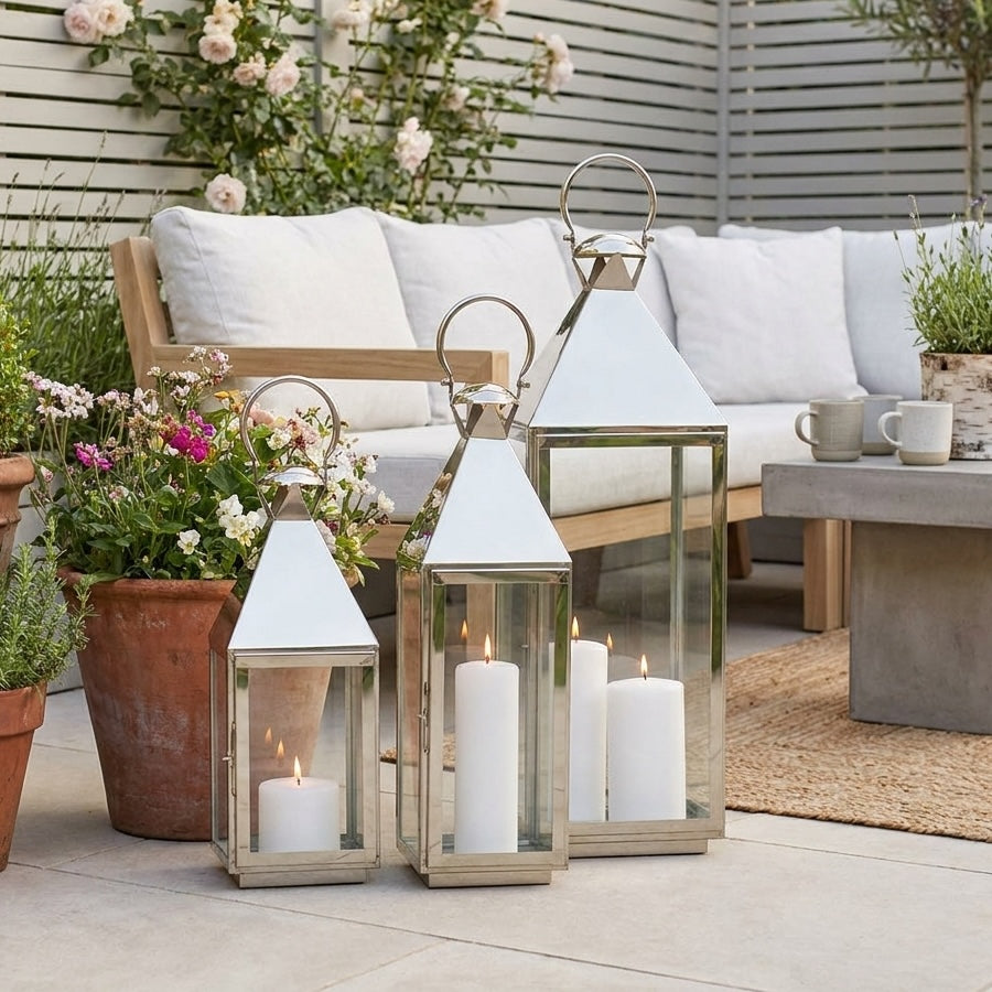Three lanterns in a garden with a olant and sofa behind