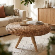 round wicker coffee table with wooden legs on a white fluffy rug in a neutral living room