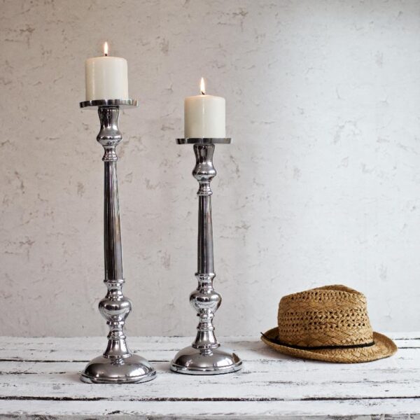 Silver pillar candle holders on white table with hat