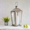 Large outdoor stainless steel candle lantern on white bench with plant and apples