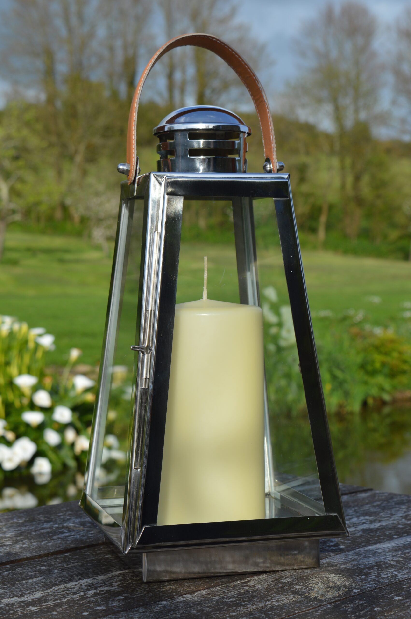 Tall outdoor stainless steel candle lantern outside with flowers