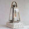 Silver lantern with leather handle on a white wicker stand