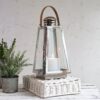 silver and glass candle lanterns on white wicker plinth with plant