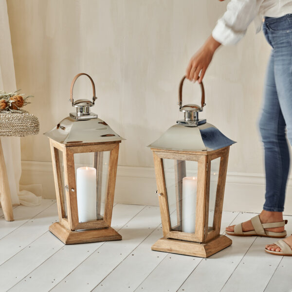 Large wood and metal candle lanterns on white wooden floor with woman holding handle