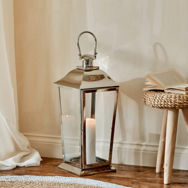 Large stainless steel lantern on wooden floor with wicker stool and rug
