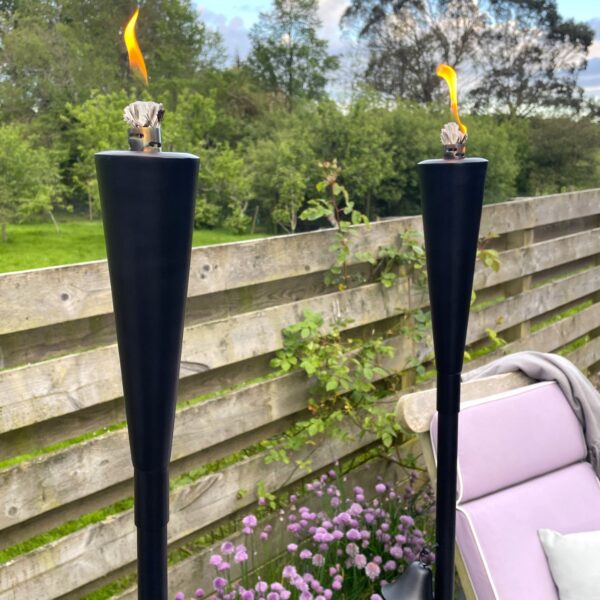 Black outdoor oil torch in garden with chair and flowers.