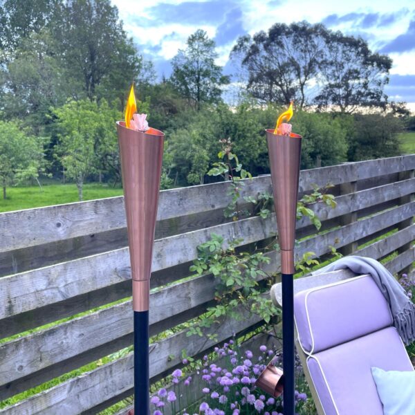 Copper garden oil torch on patio with trees and a garden chair.