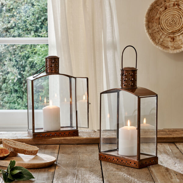 Brass and glass small candle lanterns on wooden table in front of curtain with bread on serving board