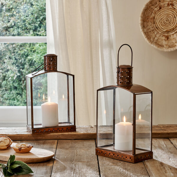 Brass and glass small candle lanterns on wooden table in front of curtain