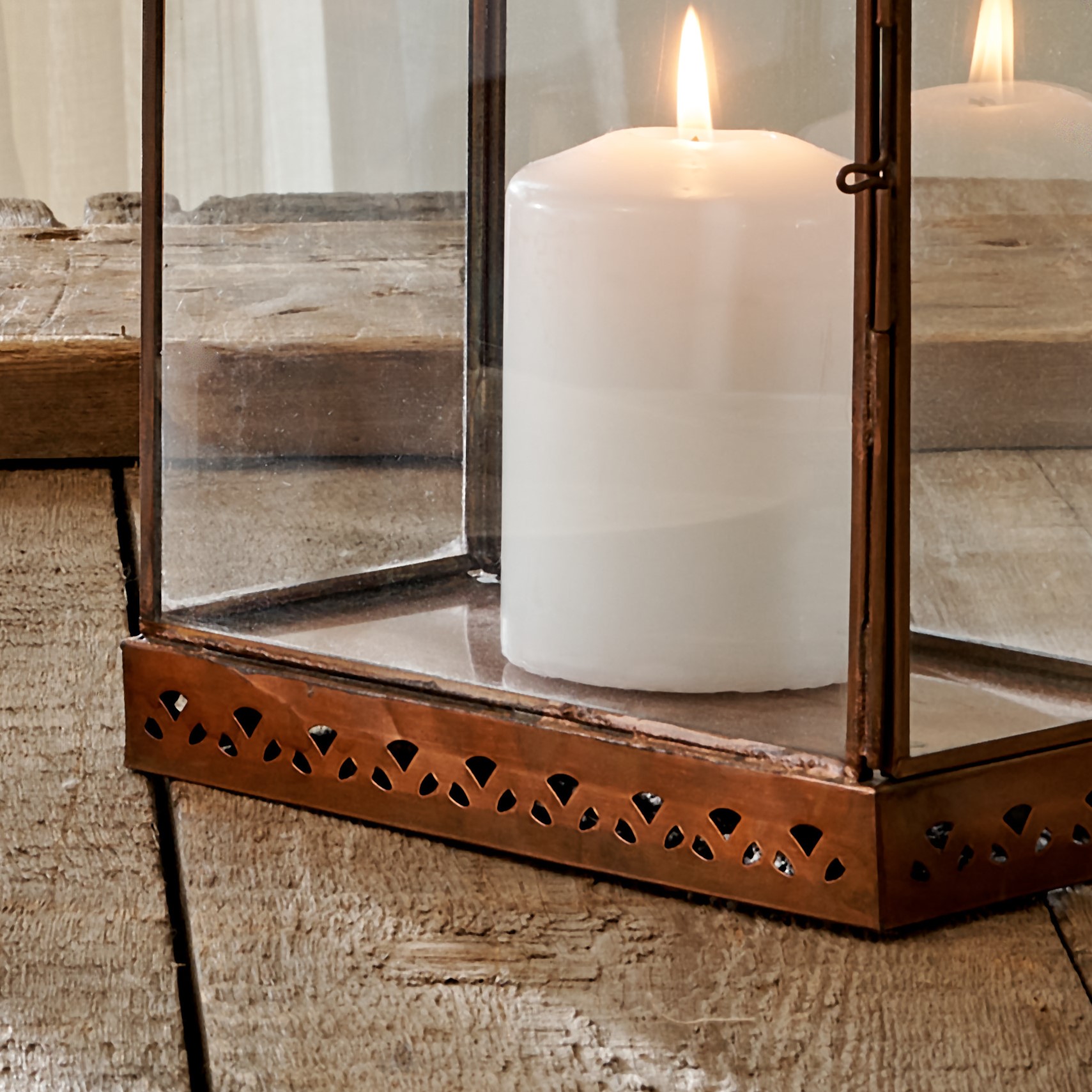 Close up of base of antique brass lantern on wooden table, with white pillar candle