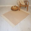 Natural cotton rug on white floor with wicker pouffe and bamboo chair