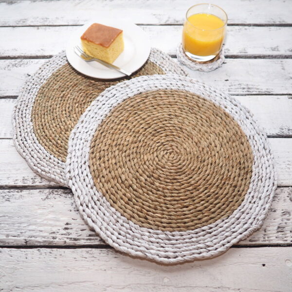 Round white wicker placemats on a white wooden table, with cake on a plate and glass of orange juice.