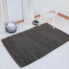Dark grey handmade woven rug Sofia on white floor with white tub chair