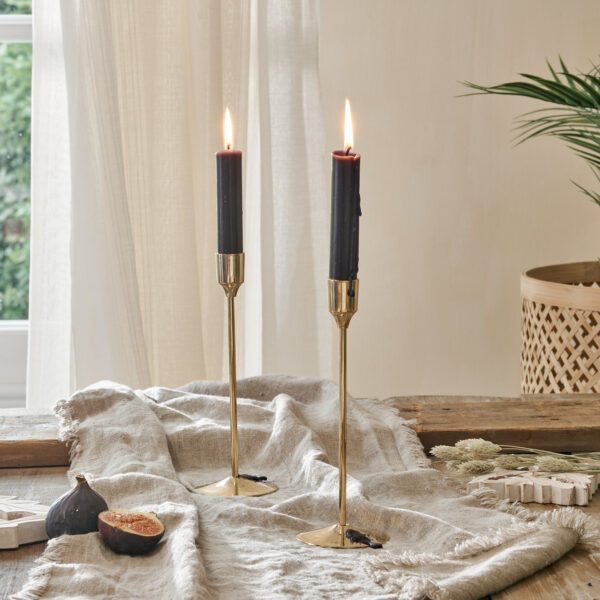 Gold candlestick holder on cotton runner on wooden table, in front of curtain with bamboo planter