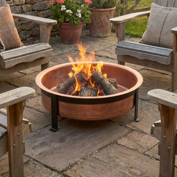 copper fire pit with logs burning on patio with chairs around