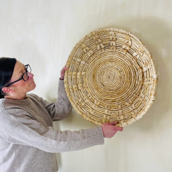 Round wicker wall art with women holding it against the wall