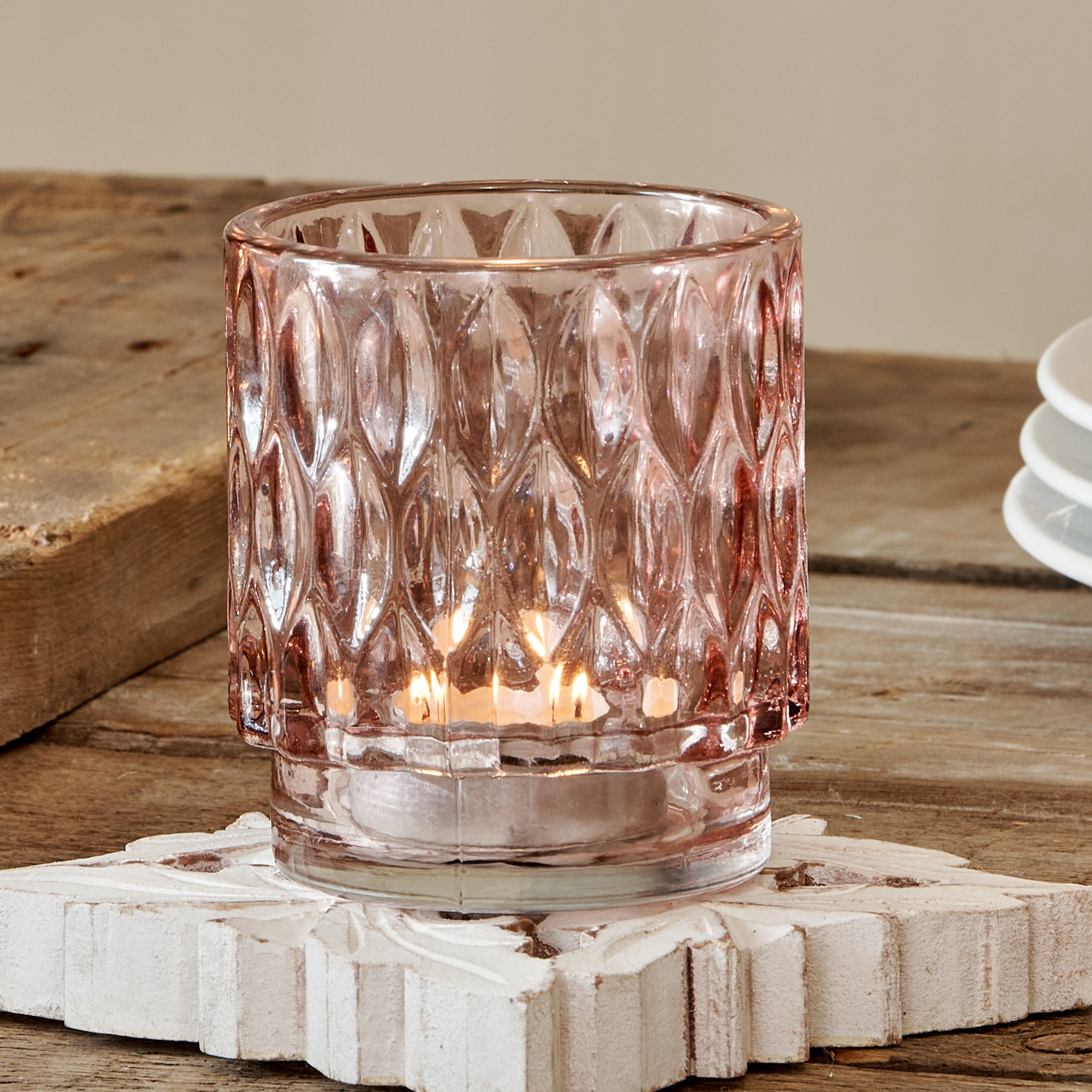 Pink glass tealight holder on white carved coaster on wooden table