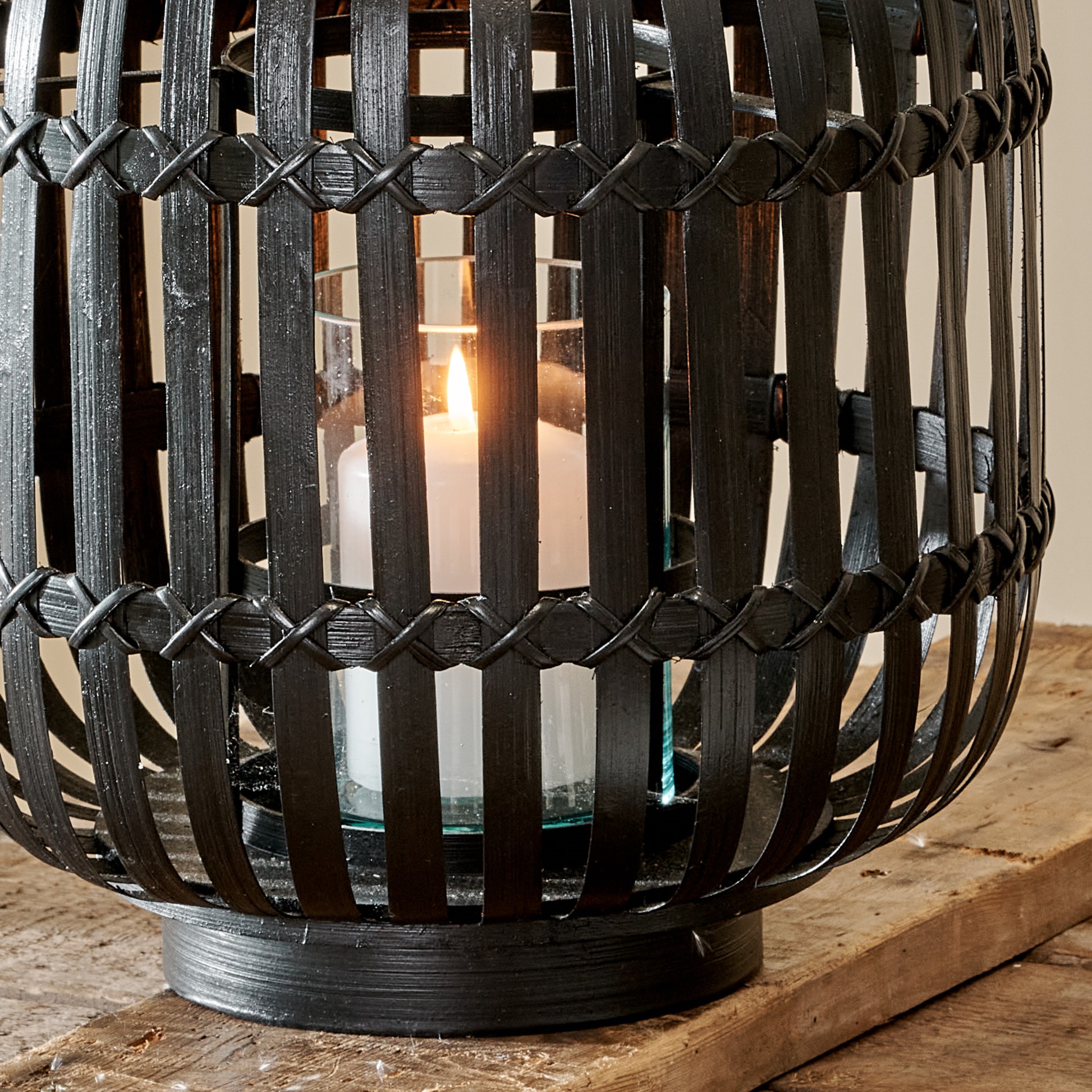 Close up of black bamboo lantern on wooden table, with white pillar candle