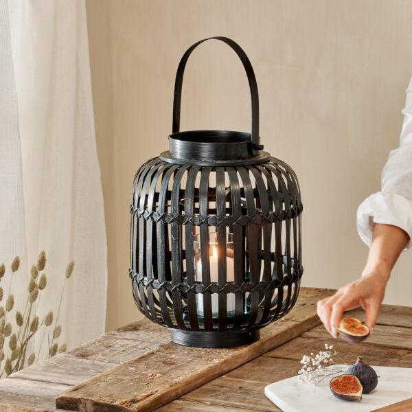 Black bamboo hurricane lantern on wooden table with woman's arm
