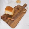 Rectangular wooden chopping board with loaf of bread and knife, on white wooden table