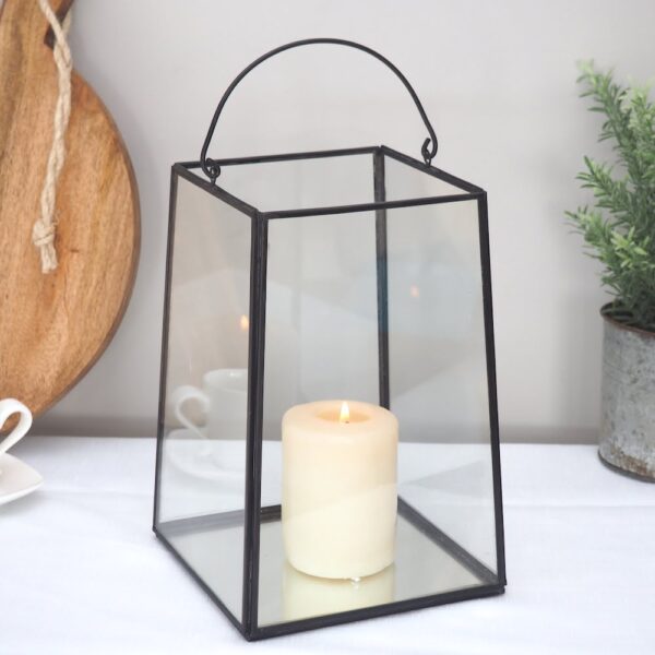 Black Metal Candle Lantern on white table with candle, with chopping board and plant pot