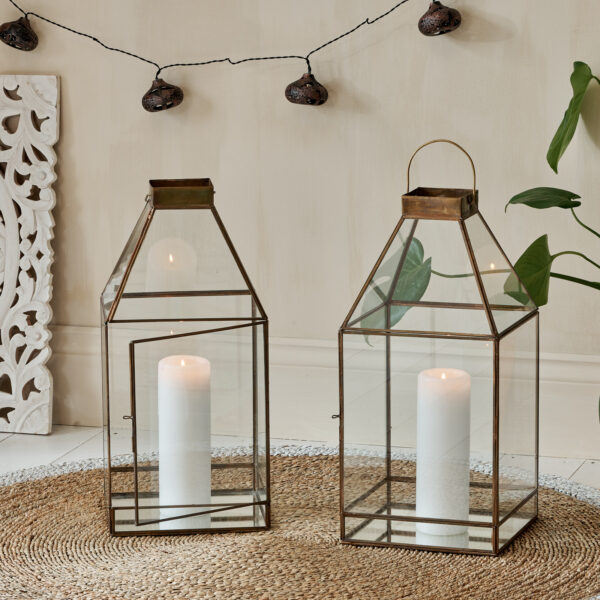 Large glass and metal candle lantern square on wicker rug, with solar lights behind