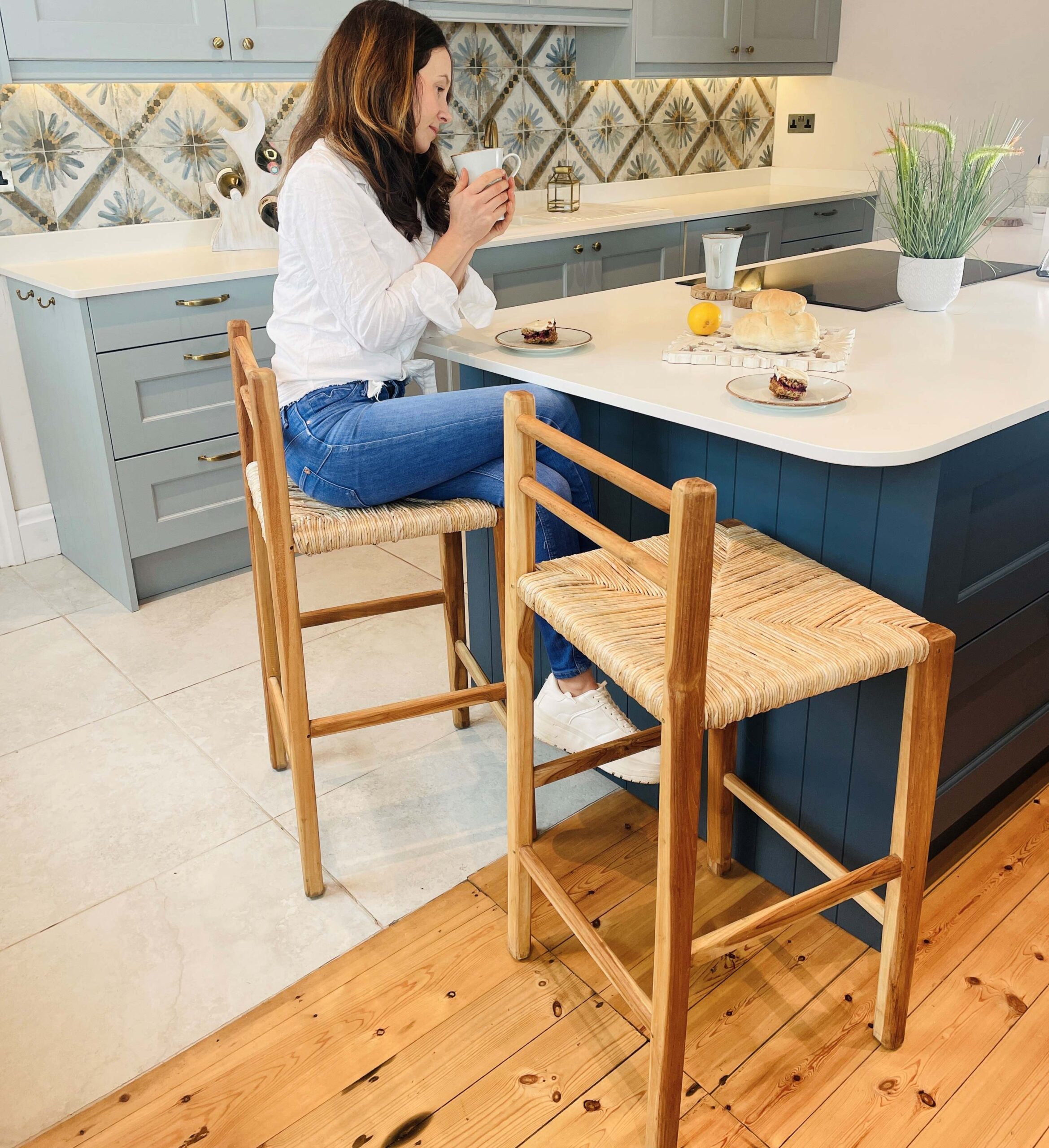 Woman sitting on wicker kitchen stool in kitchen at blue kitchen island
