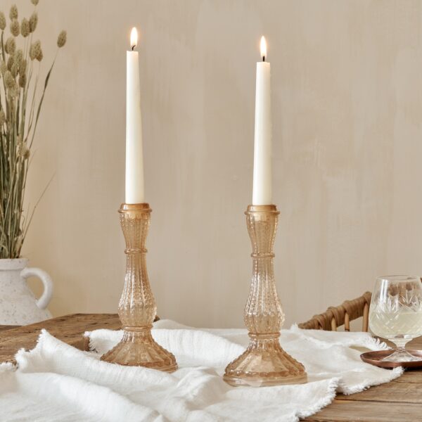 Pink candlesticks on table with grass and a glass
