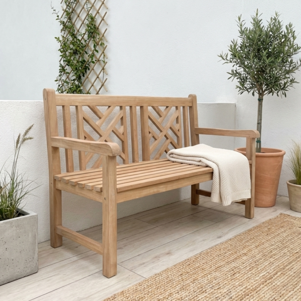 wood garden bench on garden patio with wicker rug and plants