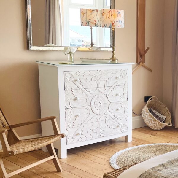 Large white chest of draws under mirror on wooden floor with lamp