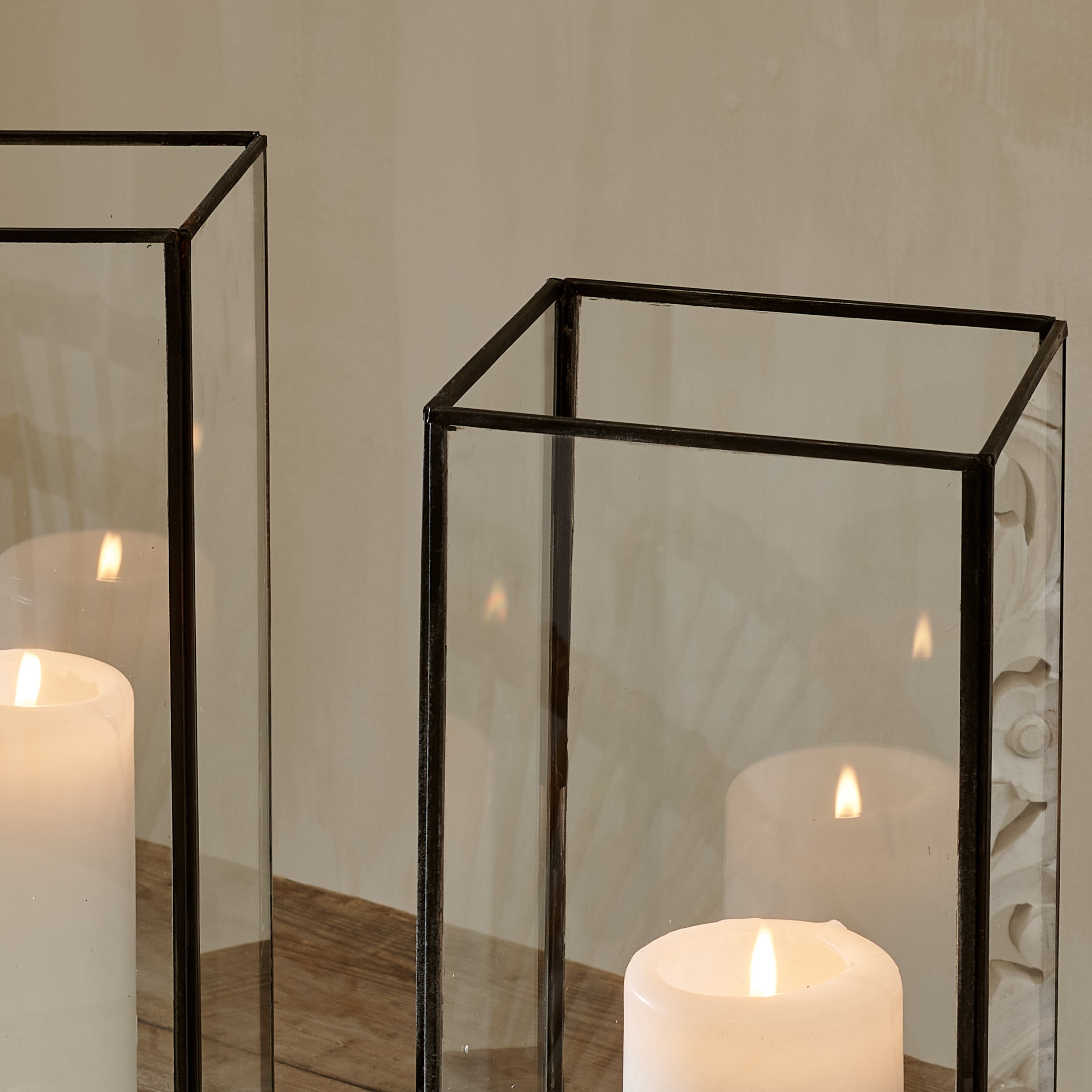 Tops of tall black candle lantern terrarium on cotton runner on wooden table