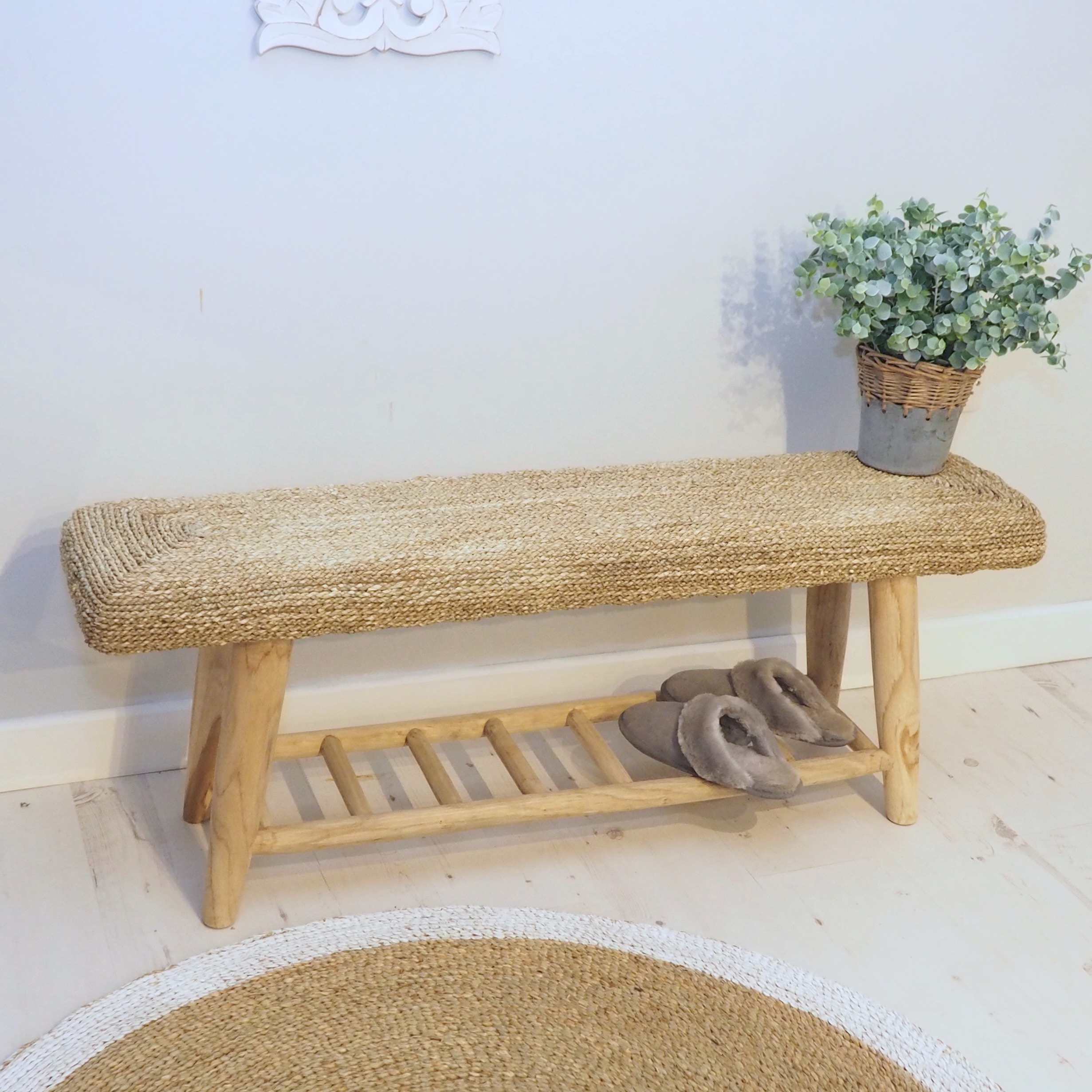 Wicker bench with shelving on wooden floor with rug, slippers and plant pot