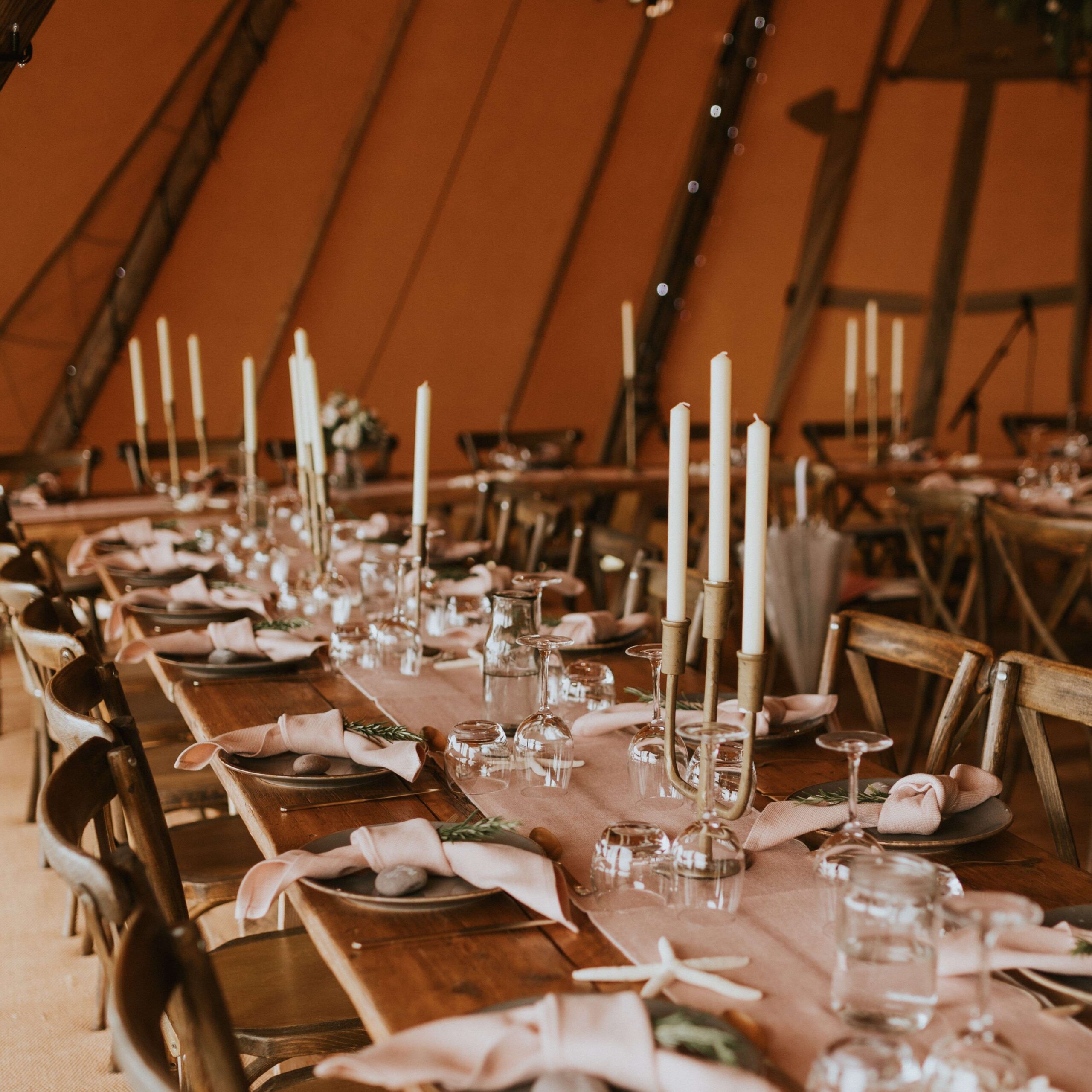 Brass candelabra on wooden wedding table place setting in orange tent