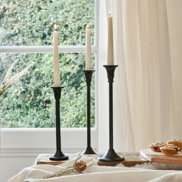 Thin black candle holders on cotton runner with mince pies, in front of curtained window