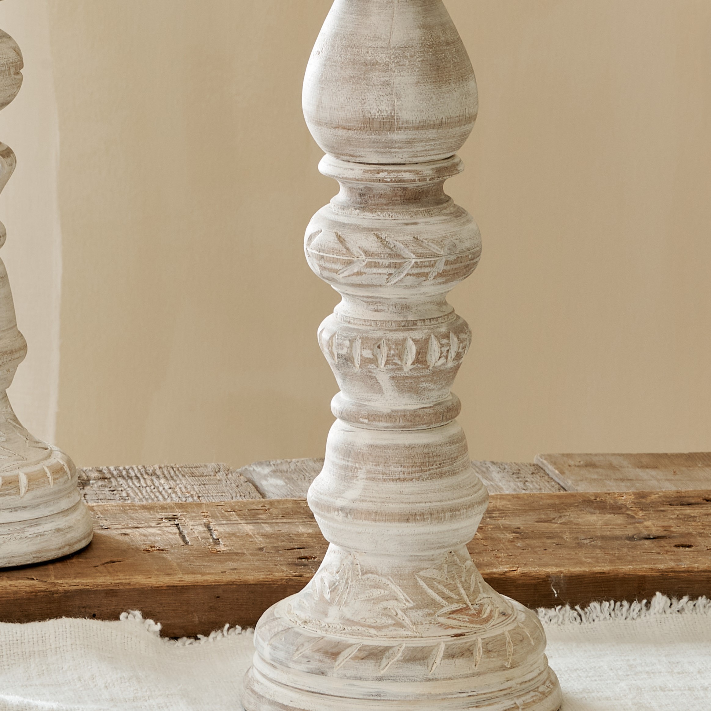 Close up of distressed tall white candlesticks on cotton runner on wooden table