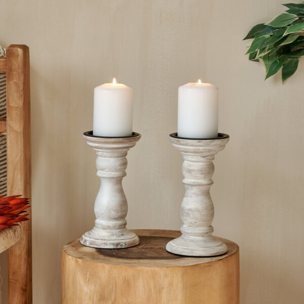 White wooden candlesticks on log table, with wooden chair and throw