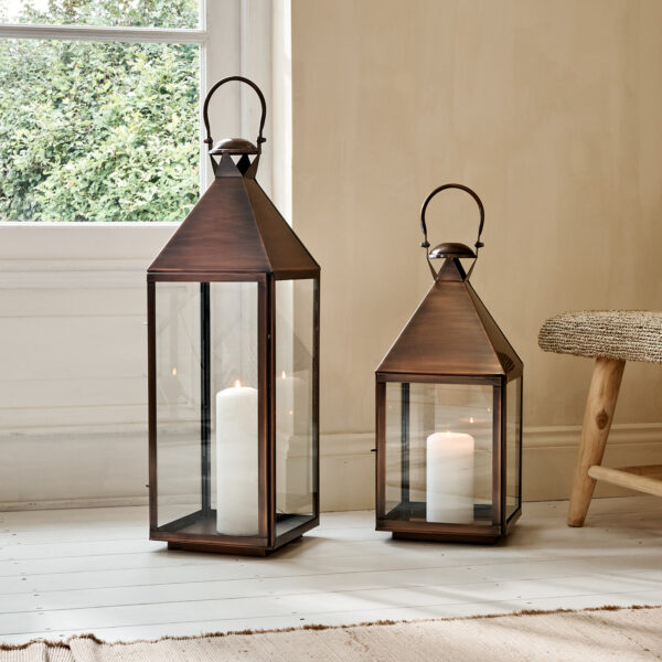 Aged copper candle lanterns on wooden floor with rug, in front of window