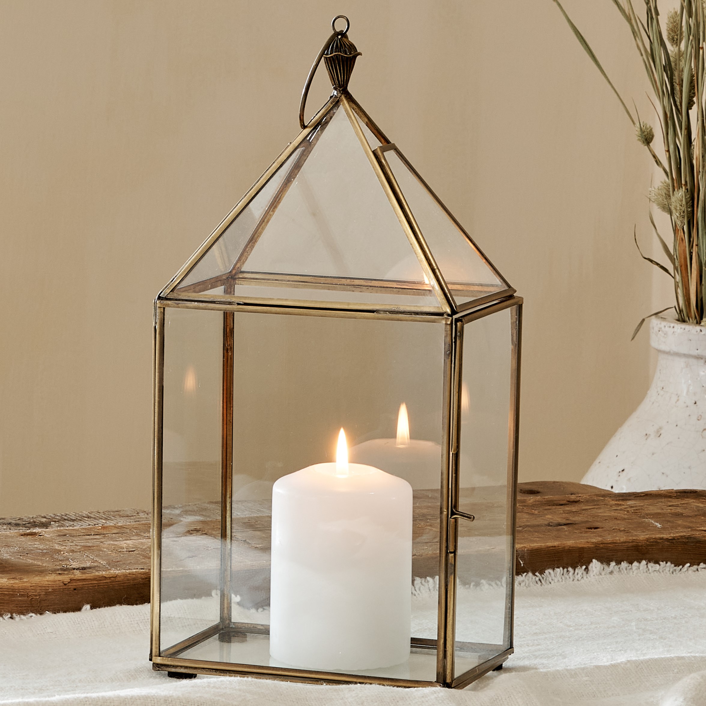 Small glass and brass candle lantern on cotton runner on wooden table