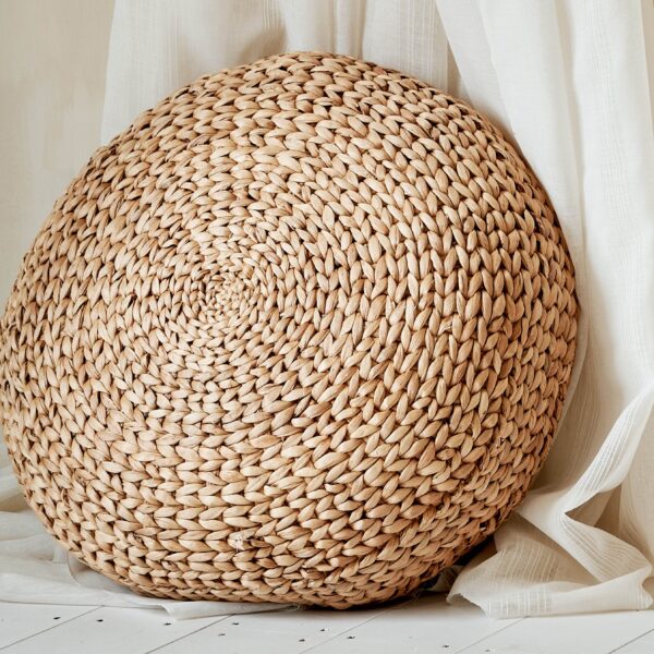 Wicker pouffe seat leant up against curtain on white wooden floor