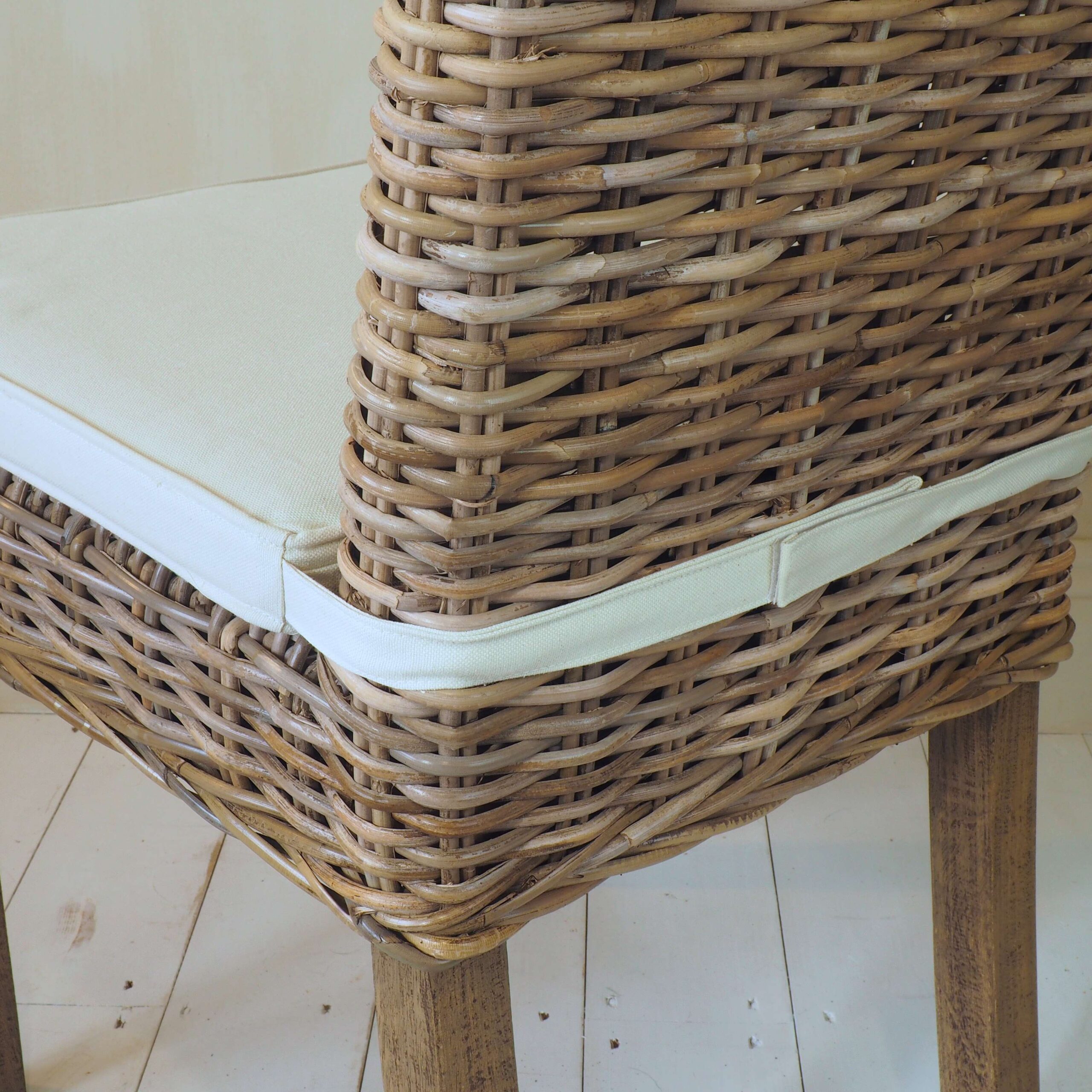 Close up of back of natural wicker dining chair, with cushion and strap