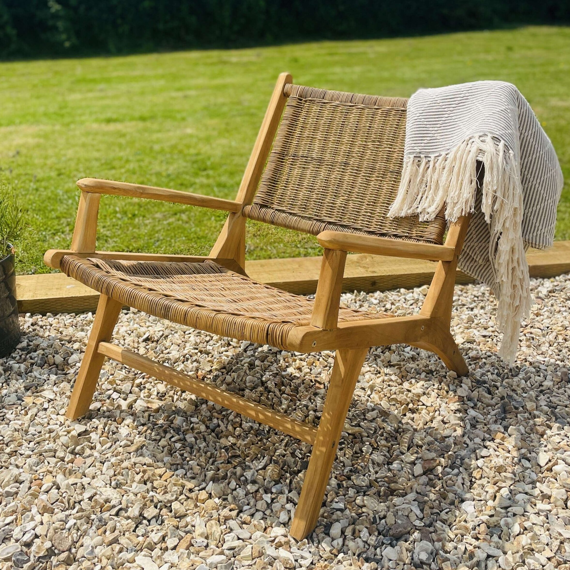 Rattan armchair with blanket in garden outdoors on gravel.