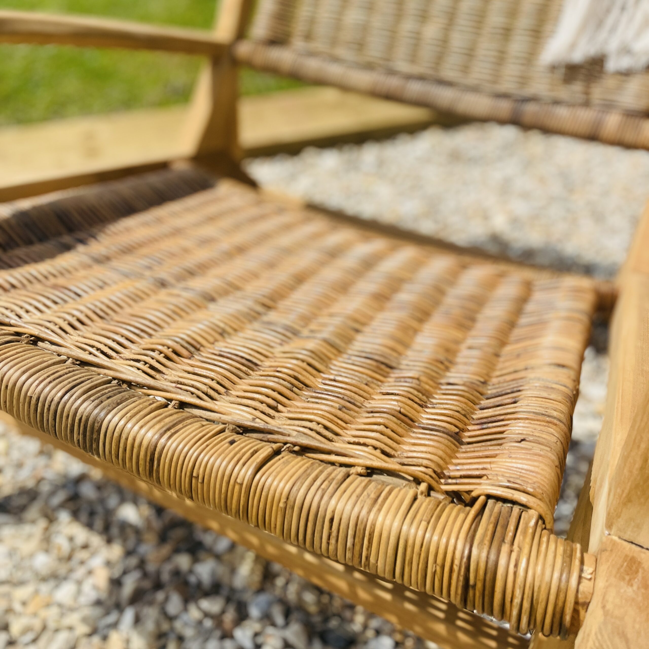 Close up of Teak Rattan Armchair in garden with grass and gravel.