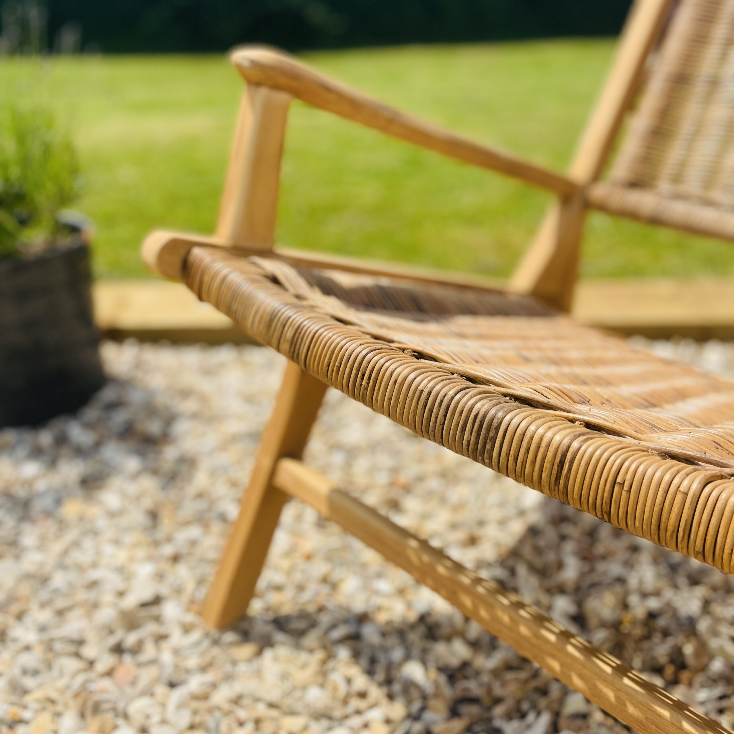 Close up image of teak rattan armchair on gravel in the garden outdoors.