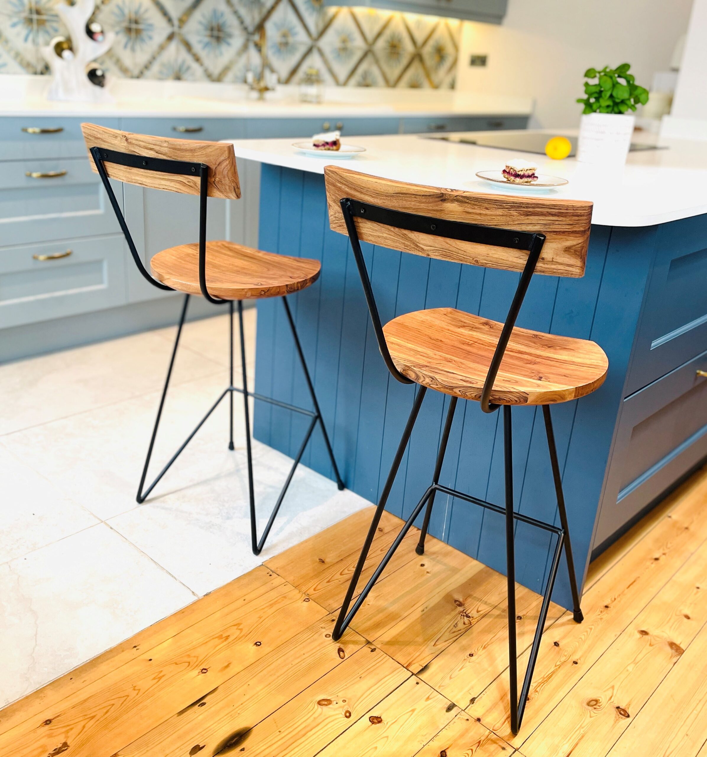 Two industrial bar stools in front of blue kitchen island on wooden floor