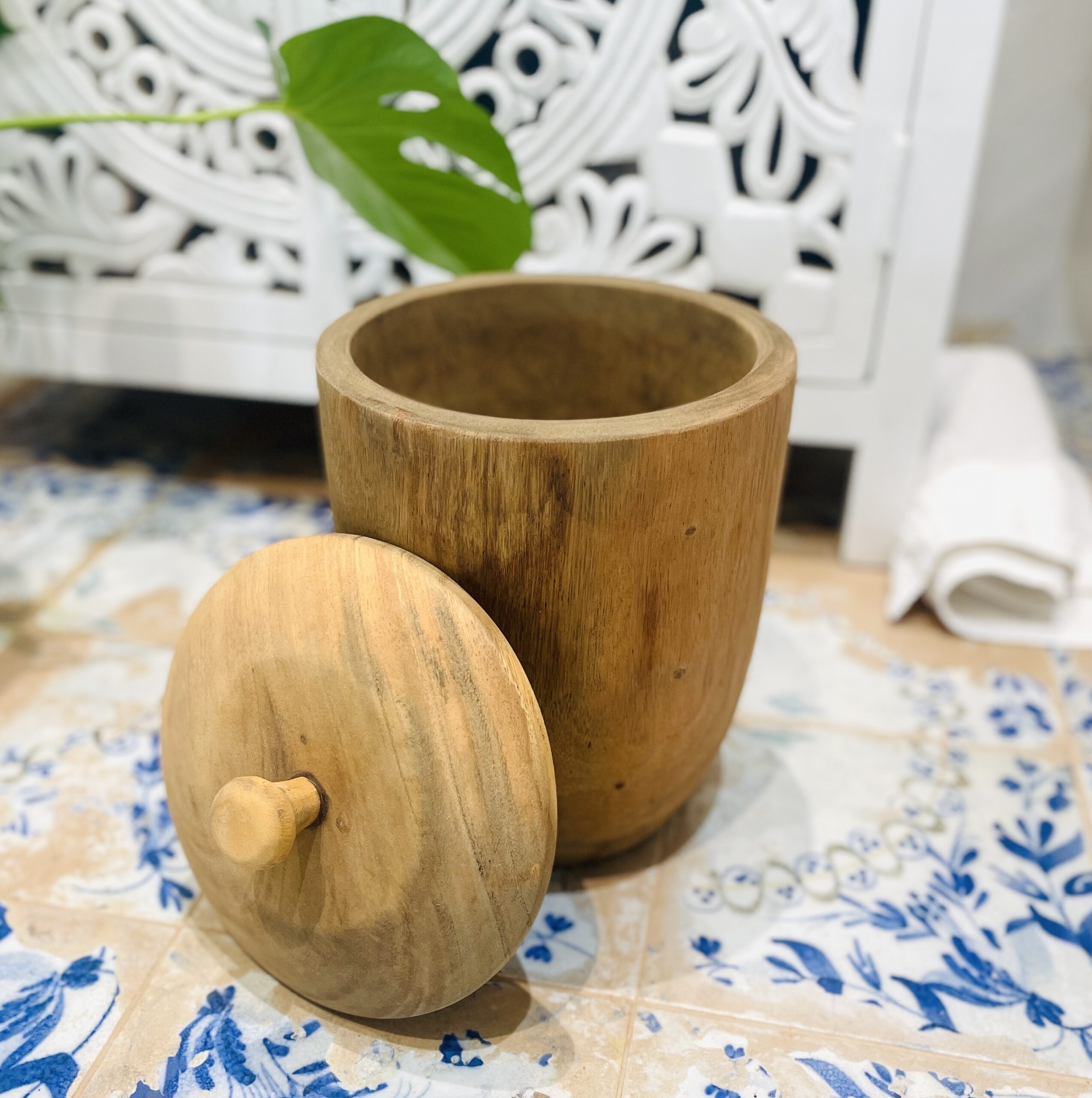 Small wooden pot with lid on side, on tiled floor in bathroom setting