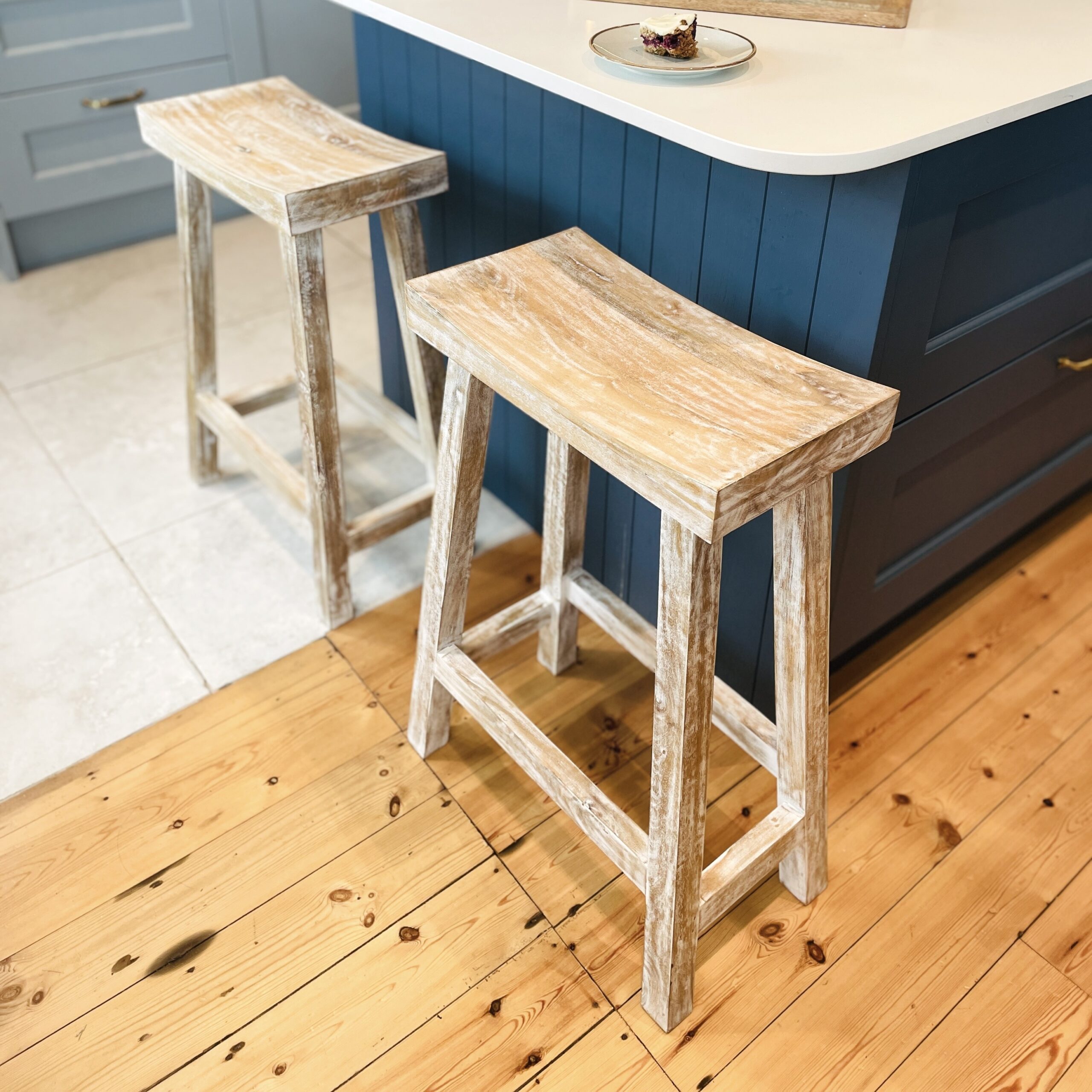 Whitewashed bar stool on wooden floor in front of blue kitchen island