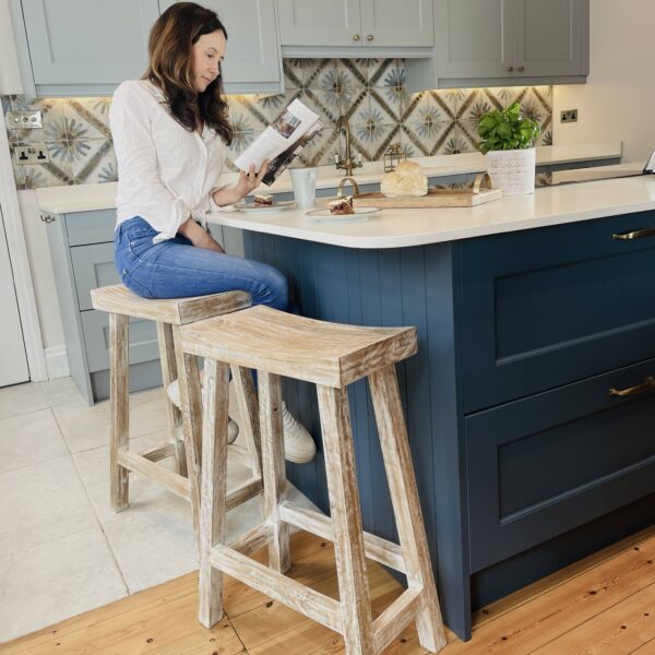 Woman sat reading on whitewashed bar stool on blue kitchen island