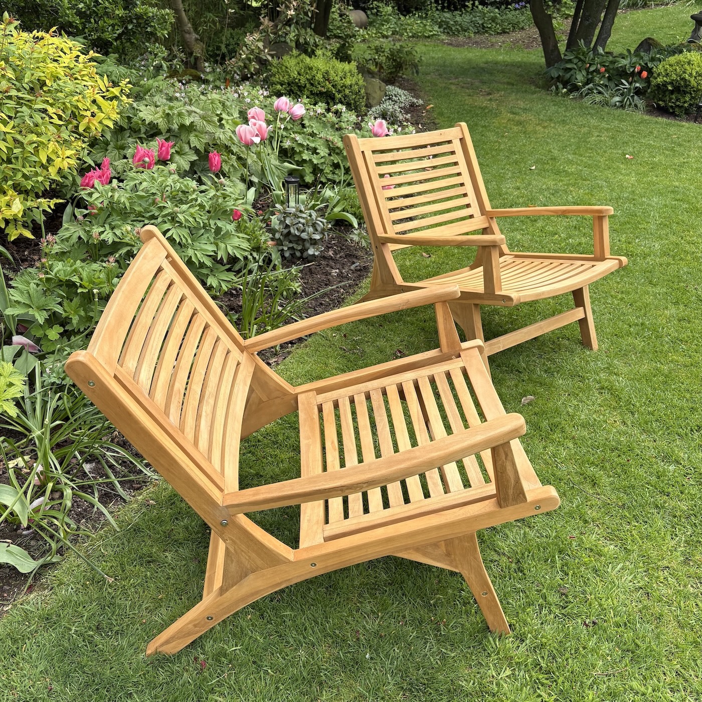 two wood garden chairs on grass with flowers in background