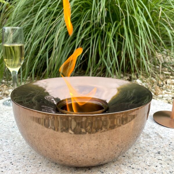 Copper gel lamp with flame in garden in front of grass and next to drinks